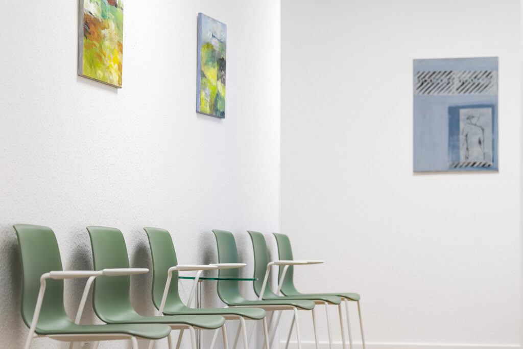 Wartebereich der Praxis mit grünen Stühlen und Bildern an der Wand